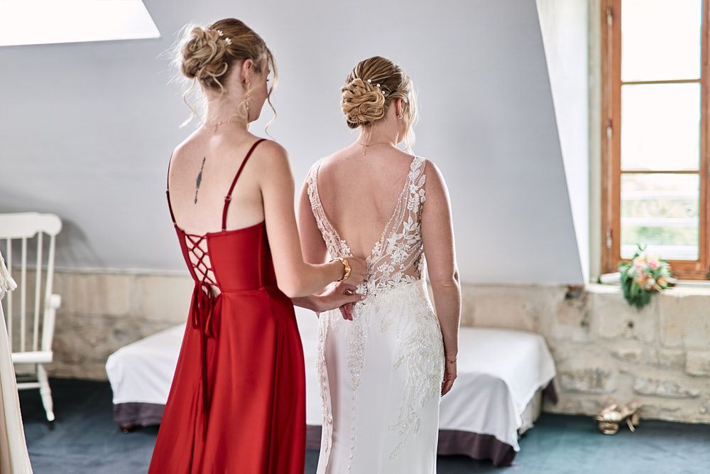 Une proche aide Harmonie à ajuster sa robe de mariée