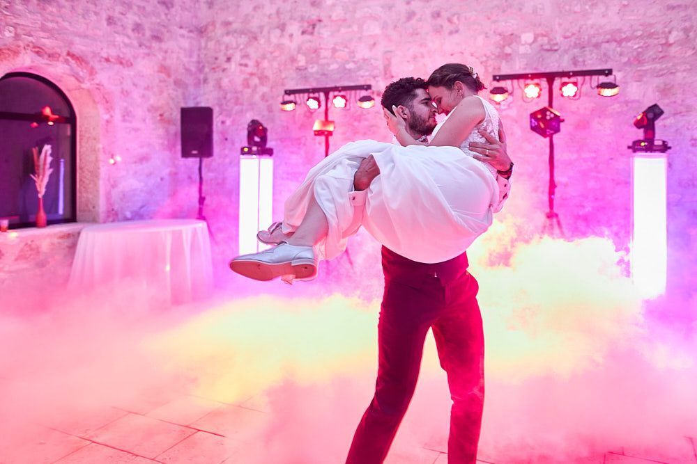 Guilhem porte Julie sur la piste de danse dans une lumière rose
