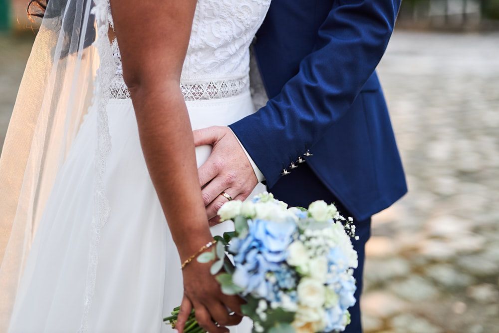Mains de Philippine et Anthony autour du bouquet de la mariée
